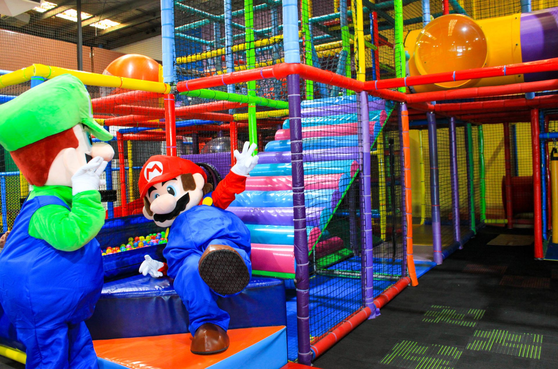 Two Mario Bros having fun in a play area, sliding down a colorful slide