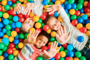 Three children laughing and having fun as they play in a colorful ball pit filled with vibrant plastic balls.