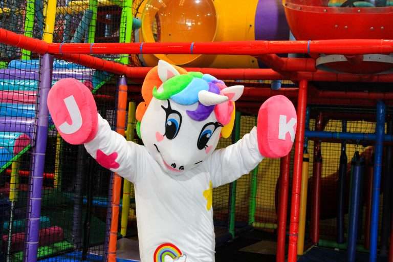 A magical unicorn mascot, surrounded by fun and laughter in a play area.