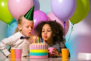 Two children joyfully blowing out candles on a birthday cake, surrounded by friends and family