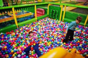 Two children joyfully playing in a colorful ball pit, surrounded by a multitude of vibrant balls.