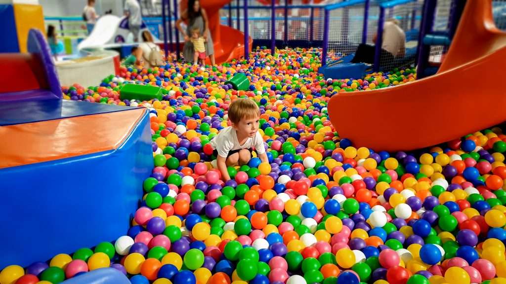 A child joyfully playing in a ball pit filled with numerous colorful balls at the main playground.